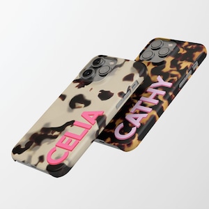 May include: Two phone cases with a tortoiseshell pattern. One case has the name "CELIA" in pink letters and the other case has the name "CATHY" in pink letters.