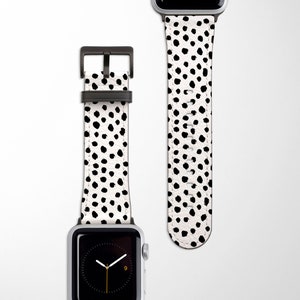 Può includere: Un cinturino per Apple Watch bianco con un motivo a pois neri. Il cinturino è in pelle e ha una fibbia nera.