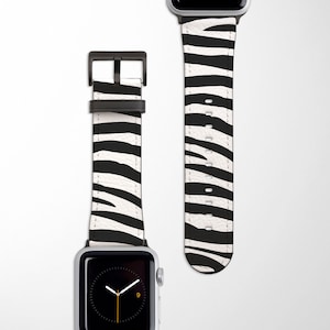 May include: A black and white zebra print Apple Watch band with a black metal buckle.