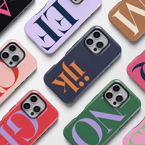 May include: Ten different phone cases with various colors and letter designs. The cases are all for the same model phone and have a raised camera bump.