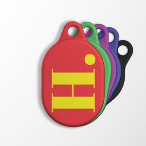 Puede incluir: Un conjunto de cinco llaveros coloridos con un llavero rojo que presenta una "H" amarilla en el centro. Los llaveros tienen forma ovalada y tienen un pequeño agujero en la parte superior para sujetarse a un llavero.