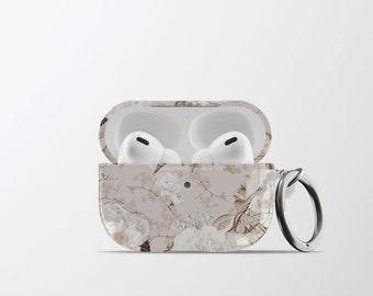 Puede incluir: Una funda blanca con estampado floral para auriculares inalámbricos con un anillo plateado. La funda está abierta y los auriculares están dentro.