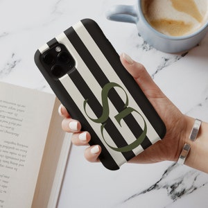 May include: A black and white striped phone case with a green letter "S" in the center. The case is made of a hard plastic material and has a raised lip around the camera lens to protect it from scratches.