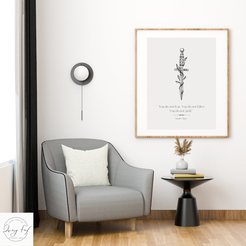 May include: A black and white illustration of a sword with vines wrapped around it. The quote "You do not fear. You do not falter. You do not yield." by Sarah J. Maas is printed below the sword. The illustration is framed and hanging on a white wall.