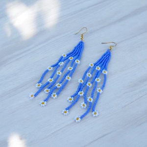 May include: A pair of long, blue beaded earrings with white daisy accents. The earrings are made with small, round beads and have a dangling design.