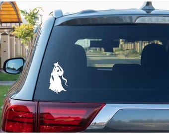 May include: A white vinyl decal applied to the rear window of a dark-colored vehicle. The decal features a silhouette of a long-haired figure in a flowing dress, depicted with arms raised above the head in a graceful, stylized pose.