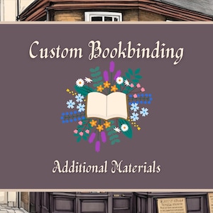 May include: A sign for custom bookbinding and additional materials. The sign is a dark purple rectangle with rounded corners. It features the words "Custom Bookbinding" and "Additional Materials" in white script. A floral wreath surrounds an open book.