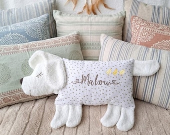 May include: A white plush dog-shaped pillow with a brown embroidered name Malow and three small gold birds. The pillow features a white fabric with small grey dots on the body and soft white textured fabric for the head, ears, and legs.