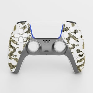 Könnte beinhalten: Ein weißer und grauer PlayStation 5-Controller mit einem goldenen und schwarzen Drachen-Design. Der Controller hat eine weiße Frontplatte mit schwarzem Rand und eine schwarze und graue Rückseite.