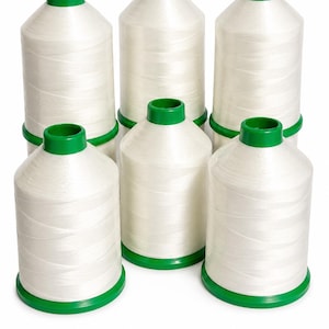 May include: A collection of six large spools of white sewing thread, each featuring a bright green plastic base and a matching green top cap. The thread is wound tightly around the cylindrical spools, creating a uniform and clean appearance.