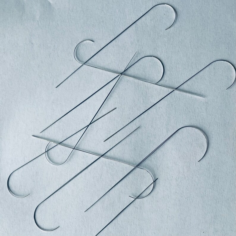 Puede incluir: Primer plano de un grupo de ganchos de metal de color plateado, algunos doblados en forma de gancho y otros rectos. Los ganchos est&aacute;n dispuestos en un patr&oacute;n aleatorio sobre una superficie azul claro.
