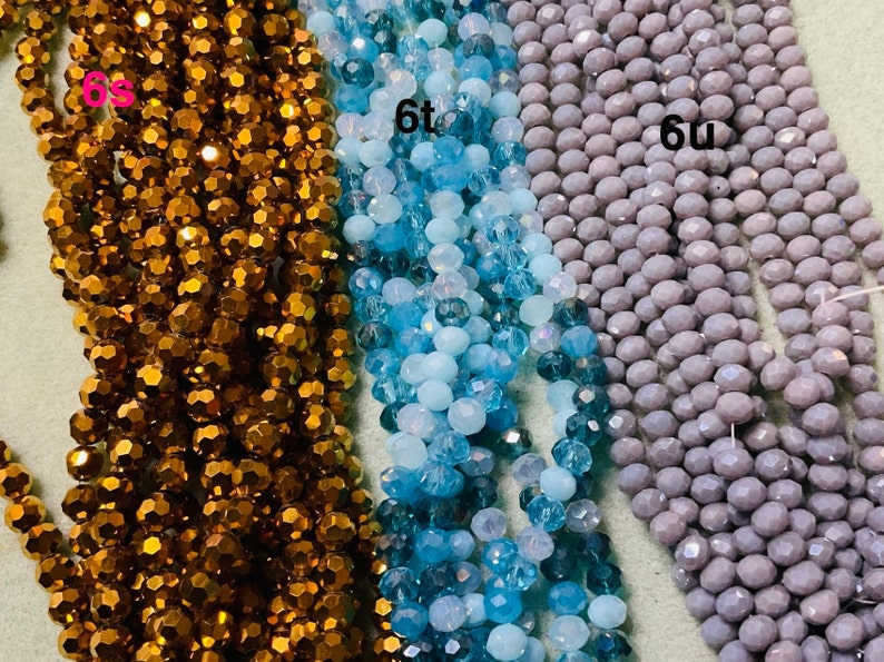 May include: Three strands of faceted glass beads. The beads are in shades of brown, blue, and grey. The strands are labelled "6s", "6t", and "6u".