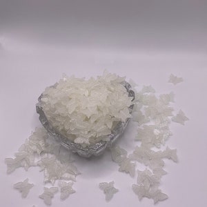 May include: A heart-shaped bowl filled with white butterfly-shaped sprinkles. The bowl is surrounded by more sprinkles on a white surface.