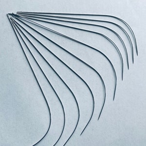 Puede incluir: Un conjunto de diez agujas curvas, dispuestas en forma de abanico sobre un fondo blanco. Las agujas son todas del mismo tama&ntilde;o y est&aacute;n hechas de metal brillante.