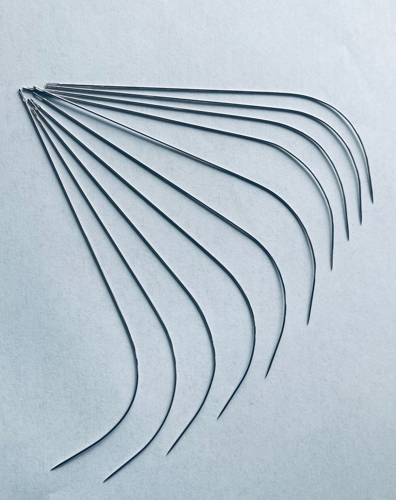 Puede incluir: Un conjunto de diez agujas curvas, dispuestas en forma de abanico sobre un fondo blanco. Las agujas son todas del mismo tama&ntilde;o y est&aacute;n hechas de metal brillante.