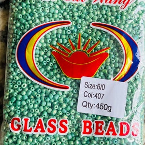 May include: A bag containing 450 grams of green glass beads, size 6/0, colour 407. The bag features a red and yellow logo with the text "Xin Cai Wang" and "GLASS BEADS". The bag also states "MADE IN CHINA".