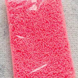 May include: A clear plastic bag filled with small, pink, round beads. The beads are opaque and have a slight shine.