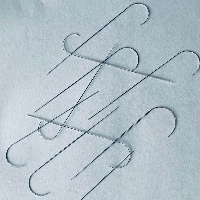 Puede incluir: Primer plano de un grupo de ganchos de metal de color plateado, algunos doblados en forma de gancho y otros rectos. Los ganchos est&aacute;n dispuestos en un patr&oacute;n aleatorio sobre una superficie azul claro.