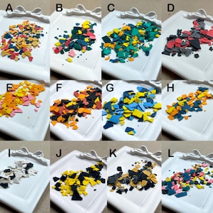 May include: A collection of colorful, irregularly shaped pieces arranged on a white, decorative tray. The pieces vary in color, including shades of orange, yellow, blue, green, and pink. The tray has a bow-shaped design on the edge.