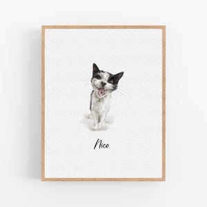 Op de afbeelding: Een aquarel van een zwart-witte kat met een speelse uitdrukking. De kat kijkt recht naar de kijker met zijn mond open. Het schilderij is ingelijst in een licht houten lijst en heeft de naam "Nico" onder de kat.