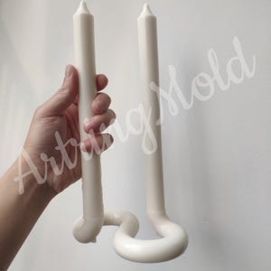 May include: Two white candles are attached to a white, curved candle holder. The holder is shaped like a double S.