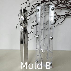 May include: A silver-coloured, twisted metal vase and a clear plastic mould with the text "Mold B". The vase has a rectangular base and a spiralling design. The mould is rectangular with metal fasteners.