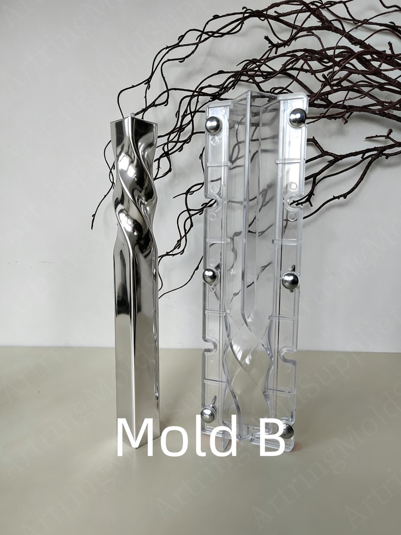 May include: A silver-coloured, twisted metal vase and a clear plastic mould with the text "Mold B". The vase has a rectangular base and a spiralling design. The mould is rectangular with metal fasteners.