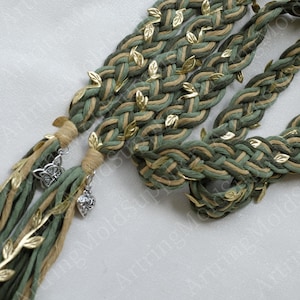 May include: Braided green and tan cord with gold leaf accents and silver charms. The cord is decorated with small gold leaves and has silver charms at the ends. The braided cord is a decorative item.