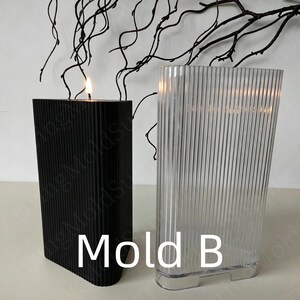 May include: A black, rectangular candle with a vertical ribbed design is lit, next to a clear, ribbed plastic mold. The text "Mold B" is printed in white. Decorative branches are in the background.