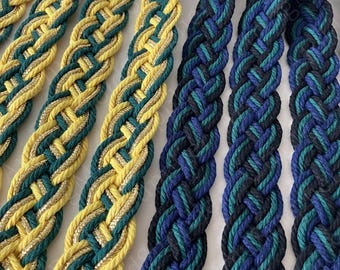 Op de afbeelding: Twee sets gevlochten koorden. Eén set bevat gele en donkergroene strengen verweven met metallic gouddraad. De tweede set bestaat uit zwarte, donkerblauwe en blauwgroene strengen die in een consistent, herhalend patroon zijn gevlochten.