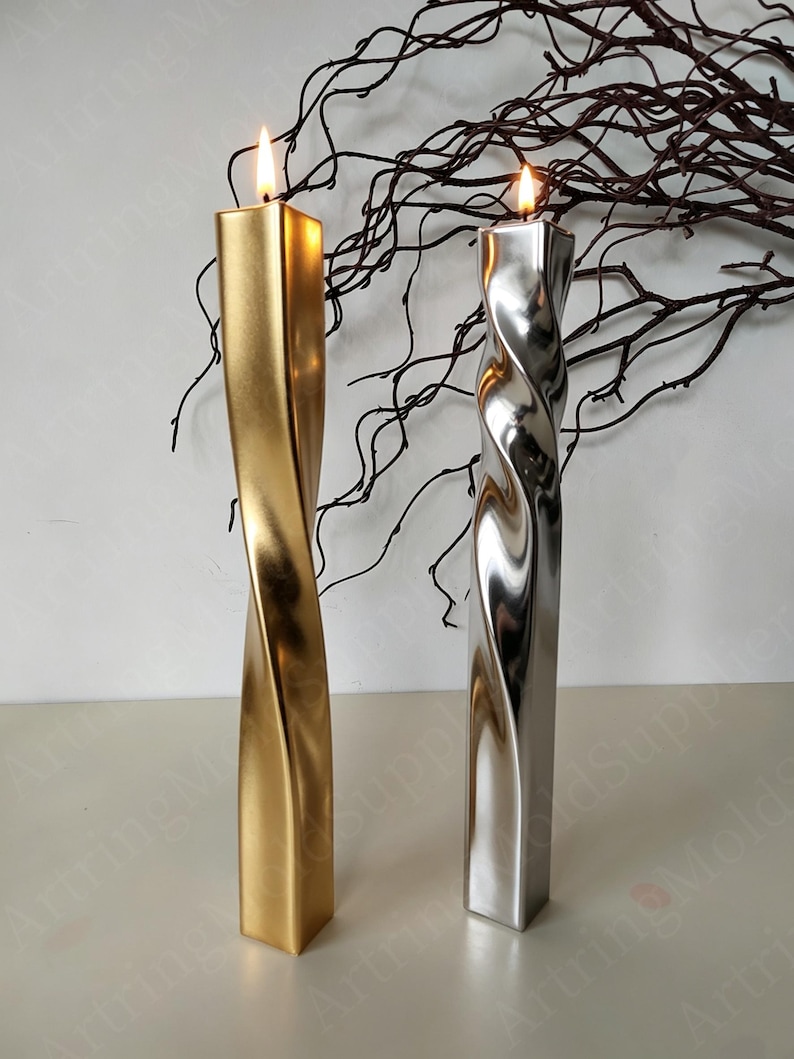 May include: Two twisted, metallic candles with lit flames. One is gold, the other silver. The candles have a square base and a spiraling design. Decorative branches are in the background.