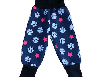Puede incluir: Pantalones azul oscuro con un patrón repetitivo de huellas de patas azul claro y pequeñas estrellas rosas. La prenda incluye una cintura elástica ancha de color negro y puños acanalados negros en los tobillos para un ajuste seguro.
