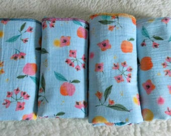 May include: Four rolled baby blankets with a light blue background. The blankets feature a repeating pattern of pink flowers, orange fruits, and green leaves. The edges of the blankets are trimmed with different colors.
