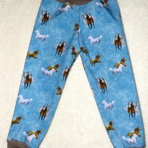 May include: Blue pants with a repeating pattern of horses in various colors. The pants have a brown waistband and cuffs. The horses are depicted in brown, white, and gold. The pants are made of a soft material.