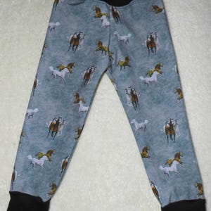 以下が含まれることがあります： 青灰色の背景に、さまざまな色の馬が繰り返し描かれたベビーパンツ。 黒いウエストバンドと袖口が付いています。 生地は柔らかく快適に見えます。