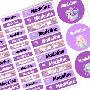 May include: A sheet of personalised adhesive labels featuring the name Madeline in black or white text. The labels include rectangular and circular shapes decorated with illustrations of mermaids, dolphins, jellyfish, and colourful fish scale patterns.