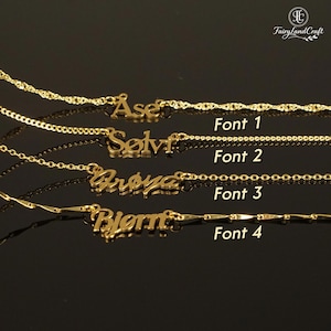 May include: Four gold-colored name necklaces displayed horizontally, each featuring a different font style labeled Font 1, Font 2, Font 3, and Font 4. The names Ase, Sølvi, Frøya, and Bjørn are written in gold metal script attached to various gold chain designs.