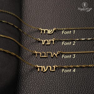 May include: Gold-colored name necklaces with Hebrew script, displayed on a dark leather-like surface. Four different fonts are shown, each with a name pendant and a delicate chain. The text "Font 1", "Font 2", "Font 3", and "Font 4" are visible.