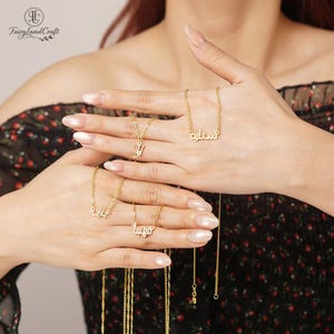 May include: Gold-colored name necklaces with Arabic script. The necklaces are displayed against a floral background. The necklaces are on delicate chains and feature different names.