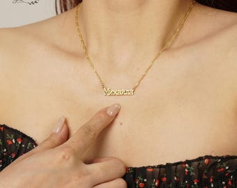 May include: A gold-colored necklace with the name "Михаила" in Cyrillic script. The necklace is displayed on a person's neck, with a delicate chain and a pendant spelling out the name. The person is wearing a black floral top.