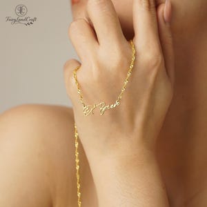 May include: A gold-colored necklace with a delicate chain and a cursive name pendant. The name "O'Brien" is displayed in elegant script. The necklace is shown against a skin tone background.