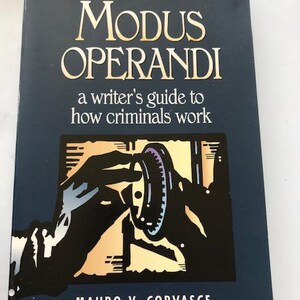 May include: A book titled "MODUS OPERANDI" from "THE HOWDUNIT SERIES" with the subtitle "a writer's guide to how criminals work." The cover is dark blue with gold lettering and an illustration of hands and a circular object. Authors are Mauro V. Corvasce and Joseph R. Paglino.