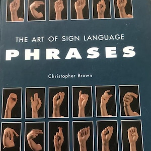 May include: The Art of Sign Language: Phrases book cover by Christopher Brown. The cover features a blue background with the title in white text and images of hands signing different phrases.