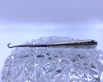 May include: A silver shoe horn with an ornate floral design. The horn is curved and has a pointed end.