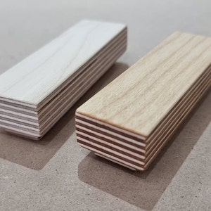 May include: Two wooden drawer pulls, one stained and one painted white. Both are made of layered wood veneer.