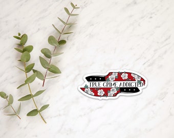 Könnte beinhalten: Ein weißer Aufkleber mit einem roten und schwarzen Messerdesign und weißen Blumen. Der Text "TRUE CRIME ADDICTED" ist auf dem Aufkleber geschrieben.