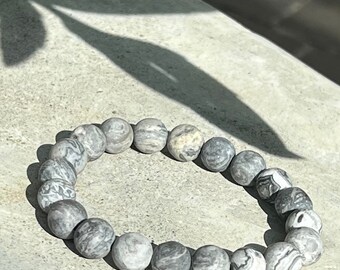 May include: A gray and white patterned stone bracelet with round beads.