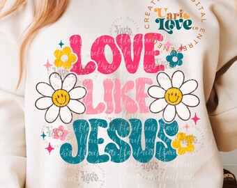 May include: A white sweatshirt featuring a graphic design that reads "Love Like Jesus" in colourful retro lettering with daisies and stars. The design has a distressed, vintage look. The text "Creative Digital Entrepreneur Vari Love Co." is in a circle on the left sleeve.