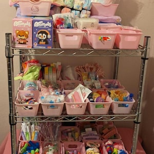 May include: A four-tier chrome wire shelving unit filled with numerous light pink plastic storage bins. The bins contain various small items including boxed toys labeled Animals, stationery, hair accessories, and colorful trinkets in clear packaging.
