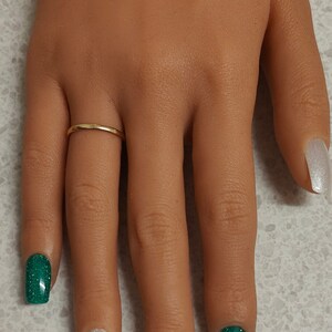 May include: A hand with five nails painted in different colours. The thumb nail is painted white with a green shamrock and the text "Happy St. Patrick's Day". The index finger nail is painted green glitter, the middle finger nail is painted gold glitter, the ring finger nail is painted green glitter, and the little finger nail is painted white.
